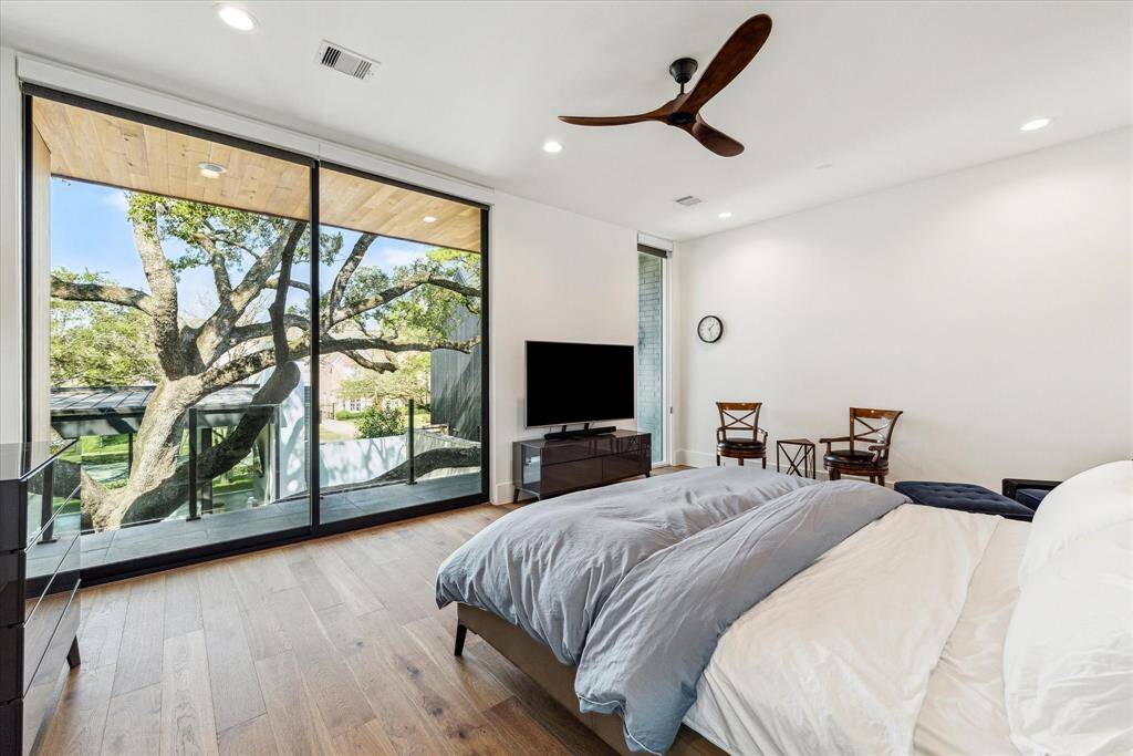 Accessed through double doors, the primary retreat is the ultimate escape. A wall of sliding glass doors opens to a private balcony, complete with automated shades for privacy and light control. The space is enhanced by wood flooring, recessed lighting, and a modern ceiling fan. With room for a comfortable sitting area, this retreat perfectly blends luxury and relaxation.