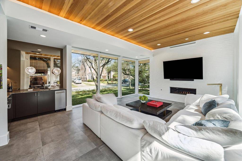 Modern elegance meets warmth in this stunning lounge, featuring a sleek wooden ceiling with cove and recessed lighting, a brick accent wall with a linear fireplace, and an entertainer’s dream bar complete with illuminated floating shelves, sink, and a KitchenAid ice maker.