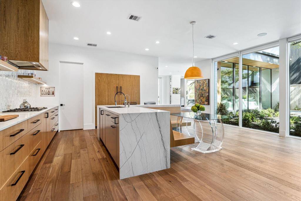 The stunning gourmet kitchen is designed for both style and functionality, featuring a central L-shaped Quartzite island with a sleek waterfall edge, breakfast bar seating, and a deep stainless steel sink with an integrated water purification system. A wall of soft-close drawers, topped with Quartzite counters, provides ample storage, while a Thermador gas cooktop, two Thermador dishwashers, and two full-size Thermador refrigerators and freezers ensure top-tier performance for culinary enthusiasts.