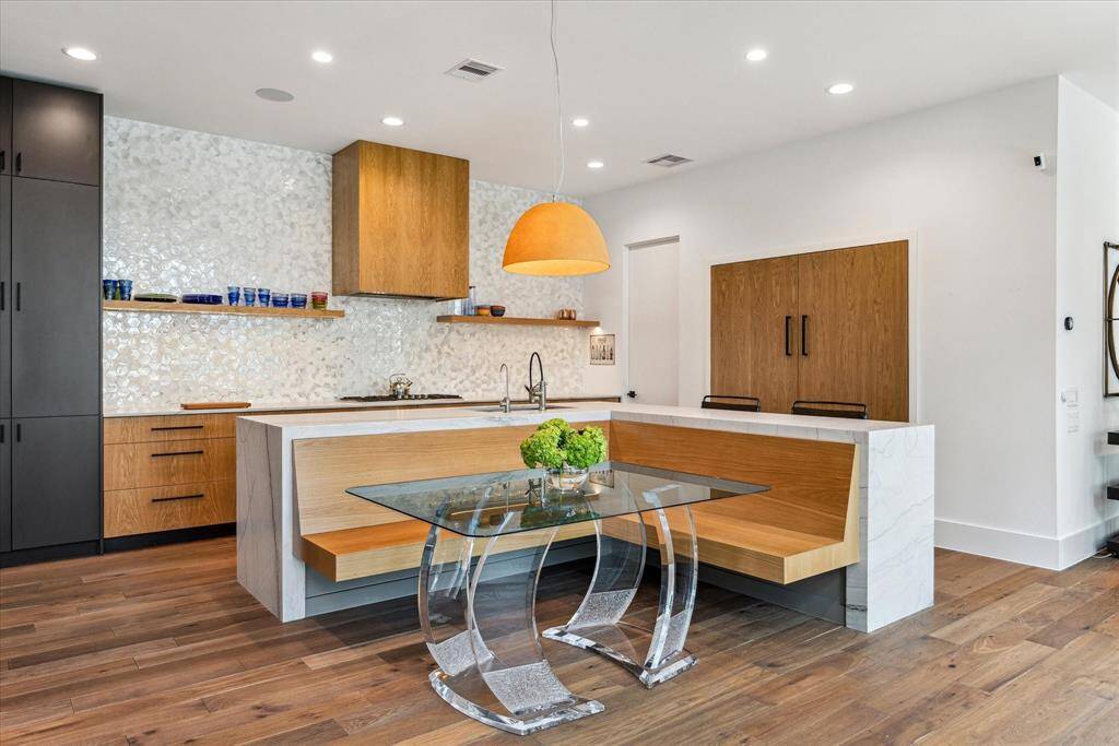 The kitchen island extends its functionality with built-in floating banquette seating, creating an inviting breakfast area. A modern dome pendant casts a warm glow above, complemented by recessed lighting and engineered hardwood flooring, which beautifully extends into the open-concept living spaces.