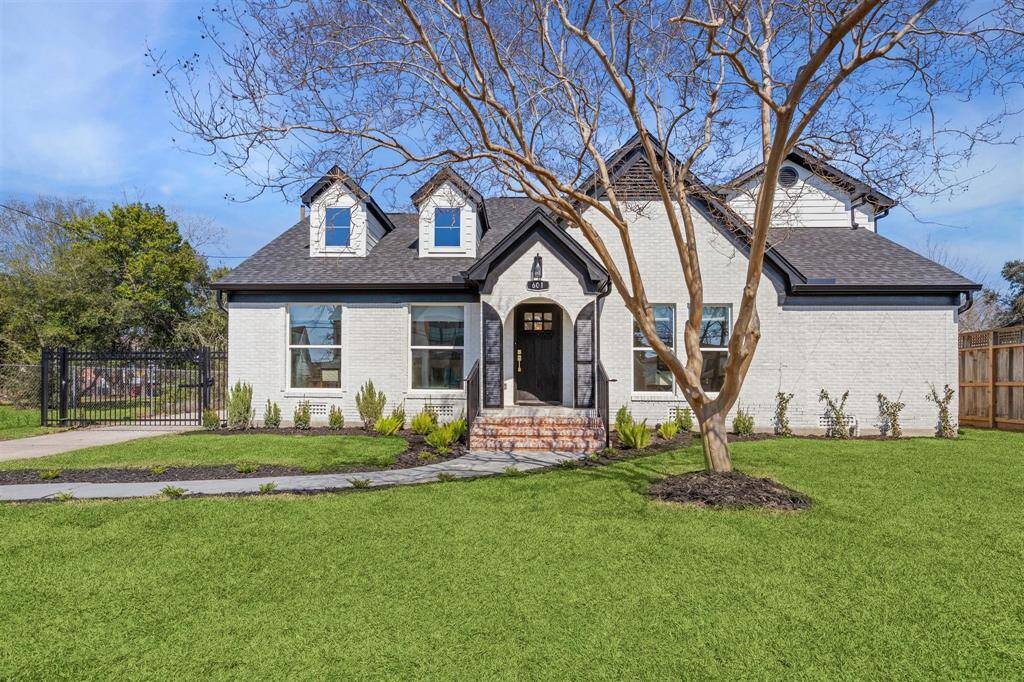 This charming home features a classic design with a white brick exterior, dormer windows, and a welcoming front porch. The spacious front yard is landscaped with a well-maintained lawn and mature trees, offering great curb appeal.