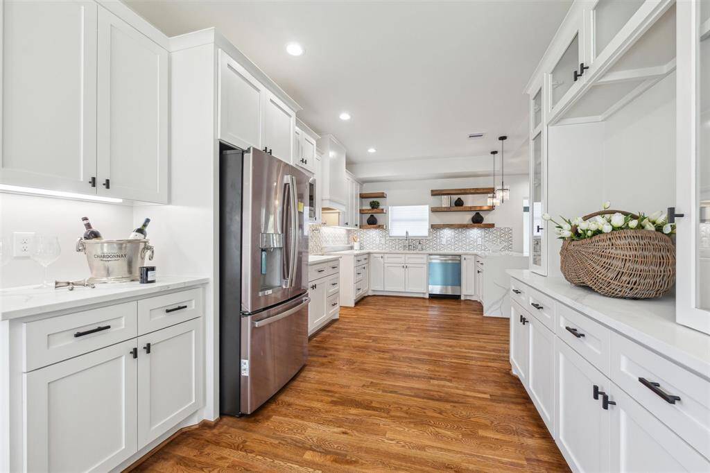 This photo showcases a spacious, modern kitchen with white cabinetry, stainless steel appliances, and hardwood flooring. It features ample counter space, open shelving, and elegant lighting, creating a bright and inviting atmosphere.