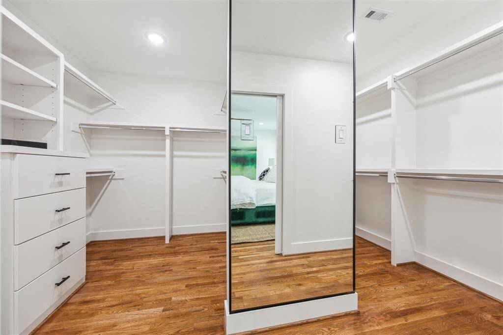 Spacious walk-in closet with ample shelving and hanging space, featuring hardwood floors and a large mirror. Perfect for organized storage and easy access to bedroom.