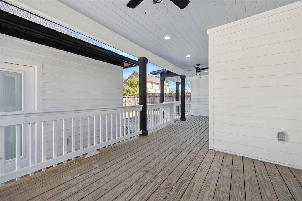 This photo showcases a spacious, covered wooden deck with a white railing, ceiling fans, and recessed lighting. It offers a cozy outdoor space, perfect for relaxing or entertaining, with a view of the backyard.