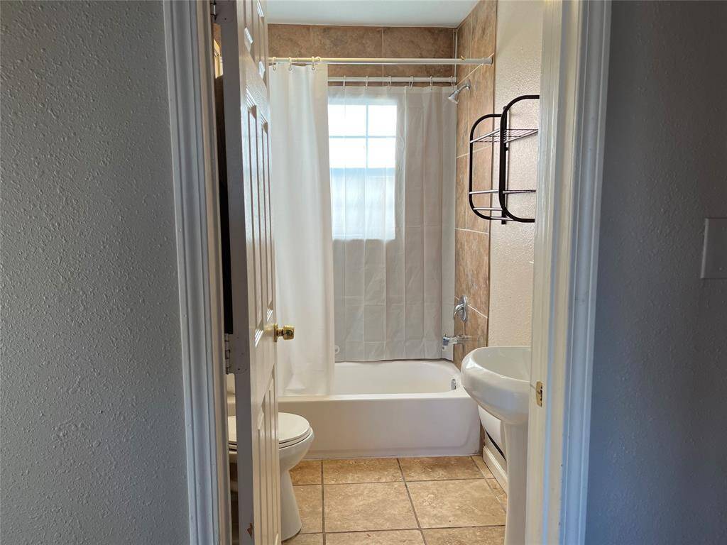 This bathroom features a tiled floor, a bathtub with a shower curtain, and a wall-mounted sink, offering a clean and simple design.
