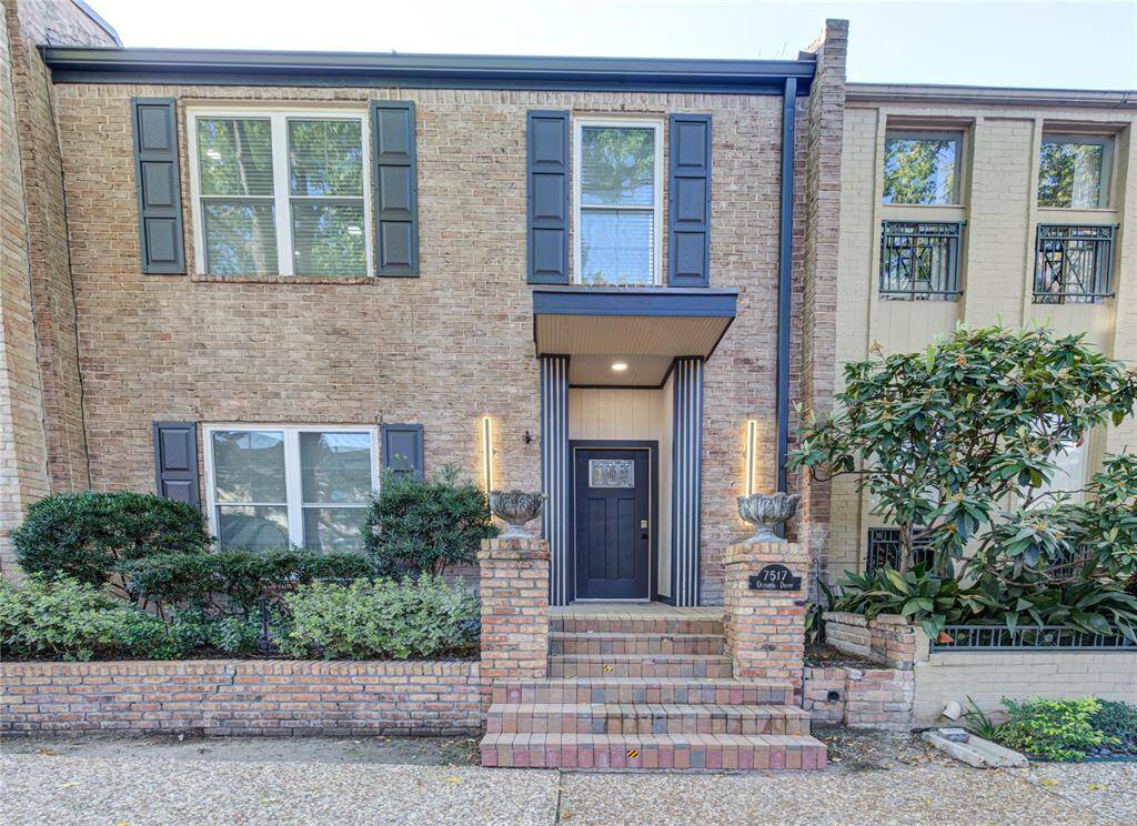 A charming two-story townhouse with a classic brick façade, framed by well-maintained landscaping and a welcoming front entrance.