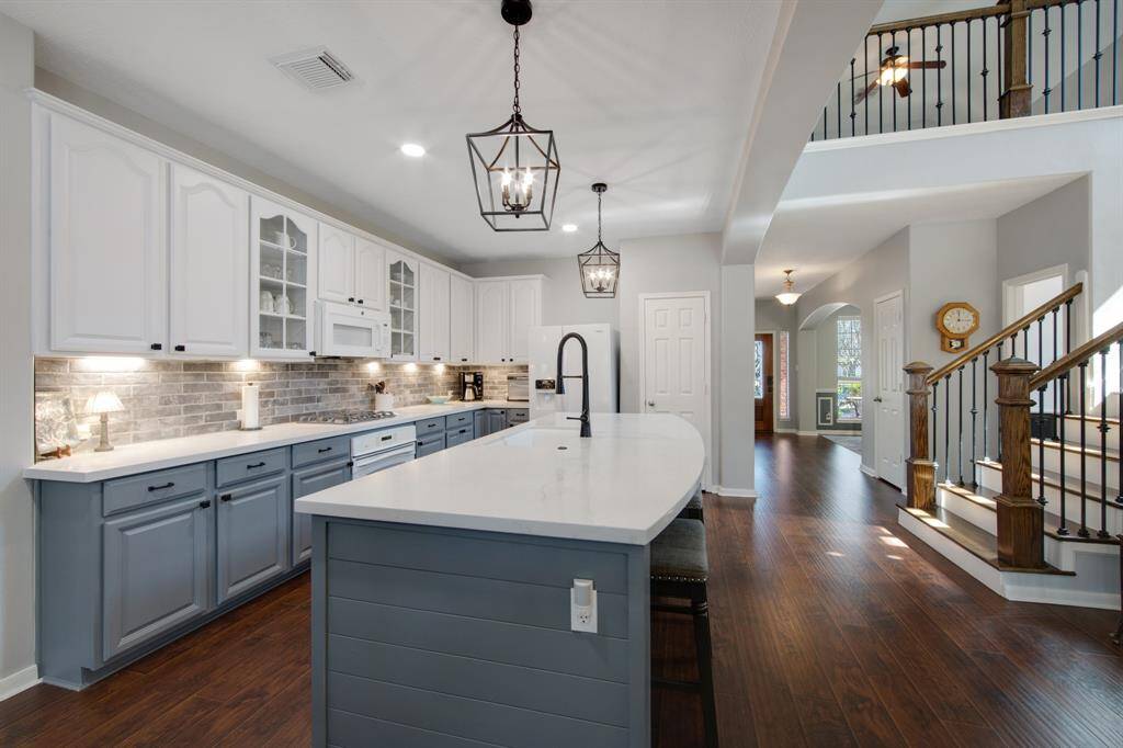 The kitchen is equipped with a gas cooktop, perfect for cooking enthusiasts who enjoy precision and control. Under-cabinet lighting adds a warm, ambient glow, while two glass-front cabinets offer a stylish display space for showcasing beautiful trinkets or glassware.