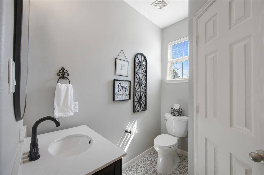 The beautiful half bathroom features gorgeous tile flooring that adds a touch of elegance, complemented by a stylish framed mirror. The thoughtfully designed space exudes charm and sophistication, making it a perfect guest bathroom.
