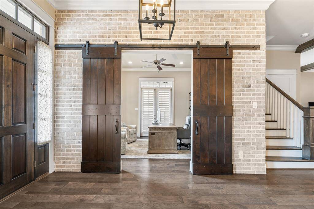 The entry opens to warm wood flooring, stylish sliding barn doors, and a stunning brick accent wall creating the perfect blend of rustic charm and modern elegance.