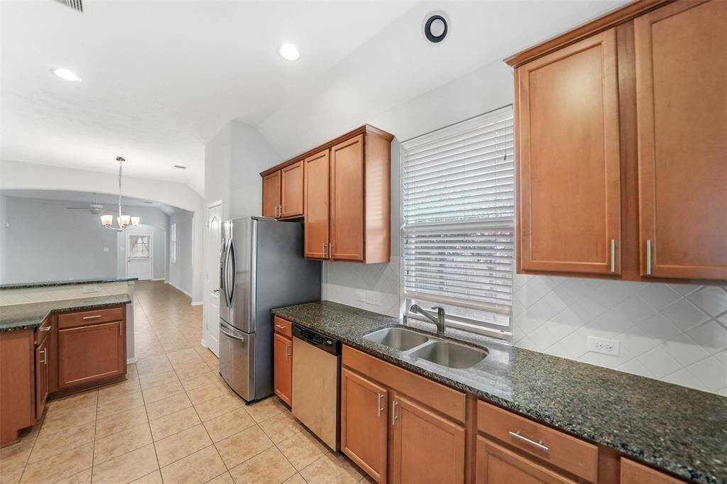 Designed for functionality and style, this kitchen features durable granite countertops, tall cabinets offering ample storage, and a large stainless steel refrigerator.