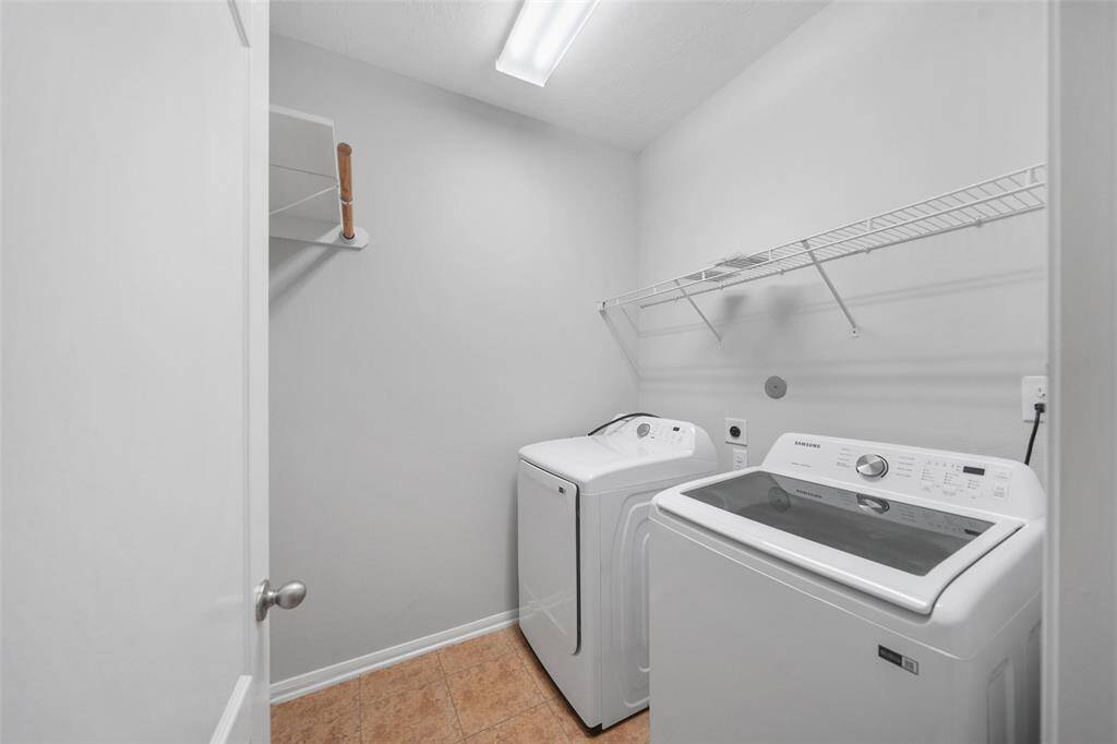 This well-lit laundry room features a full-size washer and dryer, overhead shelving for added storage, and a clean, functional layout that maximizes utility.