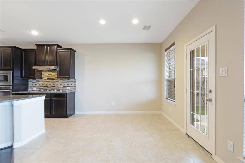 This room features a modern kitchen with dark cabinetry, a stylish tile backsplash, and granite countertops. The adjacent dining area is bright, with a large window and a glass door leading to the backyard, providing ample natural light.