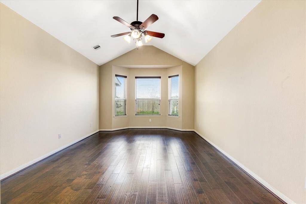 This spacious room features elegant dark wood flooring, vaulted ceilings, and a ceiling fan. Large bay windows provide plenty of natural light, creating a bright and inviting atmosphere.