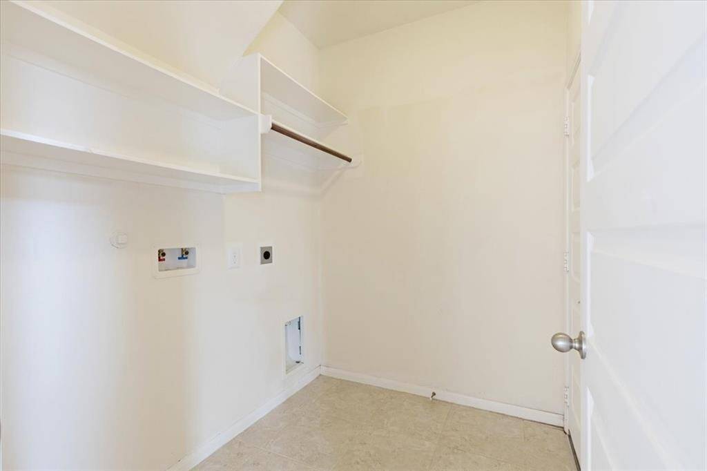 This photo shows a utility room with hookups for a washer and dryer. It features white walls, tile flooring, and open shelving for storage.