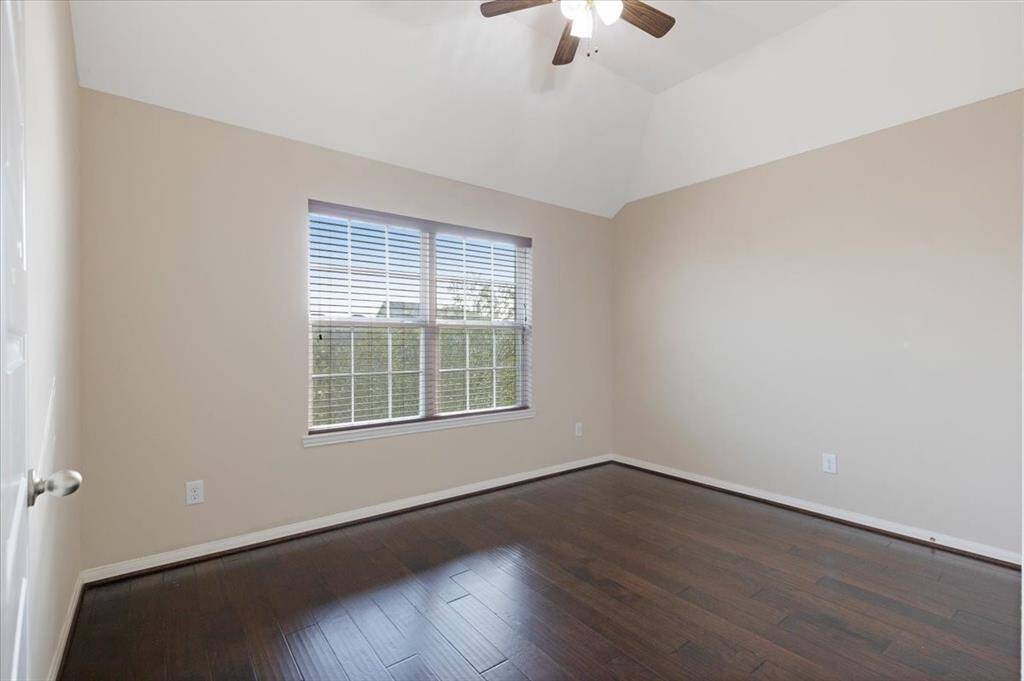 This room features neutral walls, dark hardwood flooring, and a ceiling fan. A large window provides ample natural light, creating a bright and welcoming space.