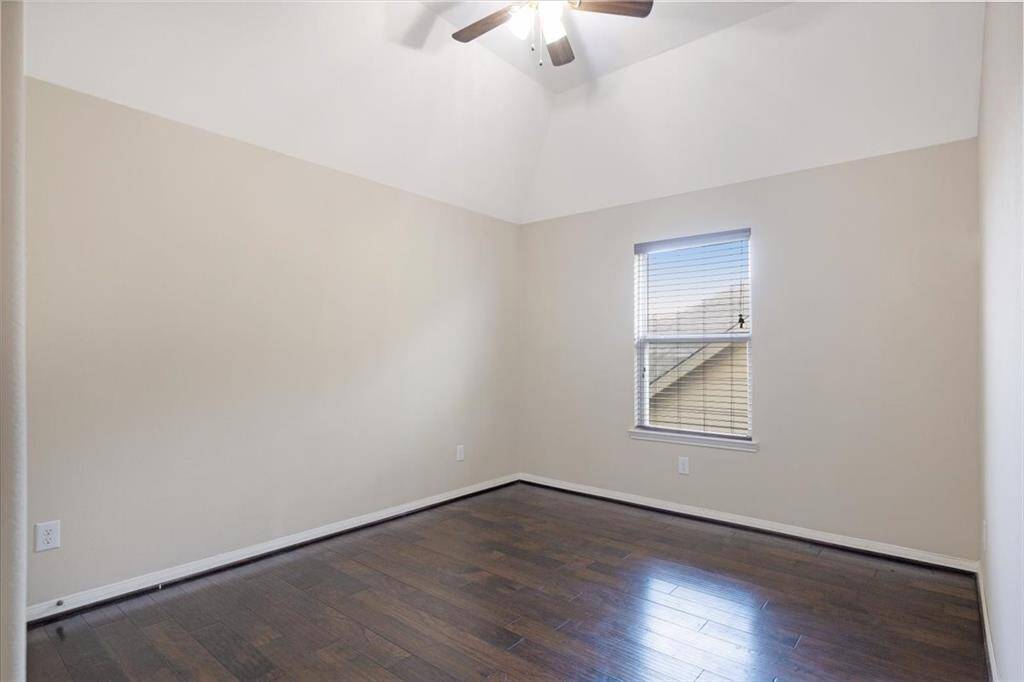 This room features neutral walls, dark hardwood floors, and a ceiling fan. A single window allows natural light, making it ideal for a bedroom or office space.
