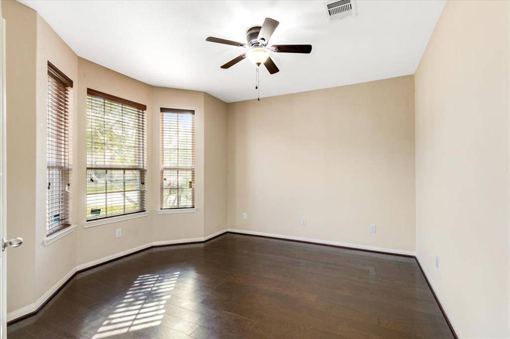 This room features warm beige walls and dark wood flooring, complemented by a ceiling fan. Large bay windows provide ample natural light, creating a bright and inviting space.