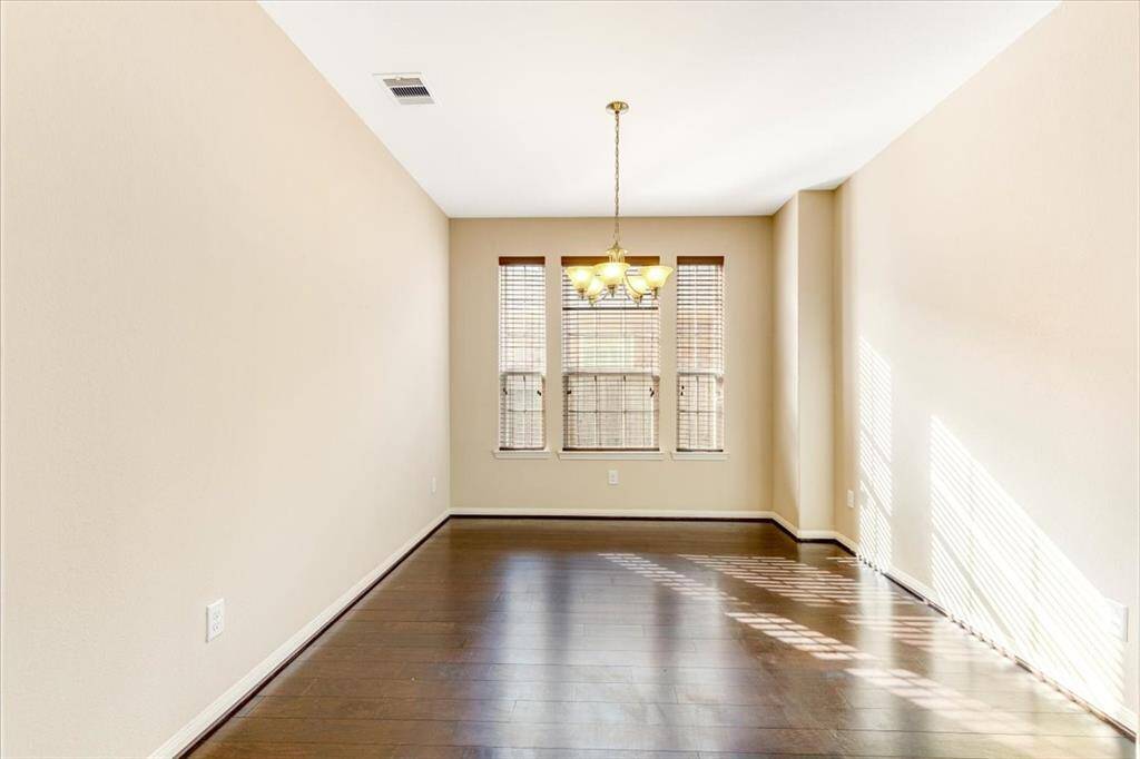 Bright dining area with dark wood flooring, neutral walls, and three large windows that let in plenty of natural light. Features a central chandelier and a clean, modern design.