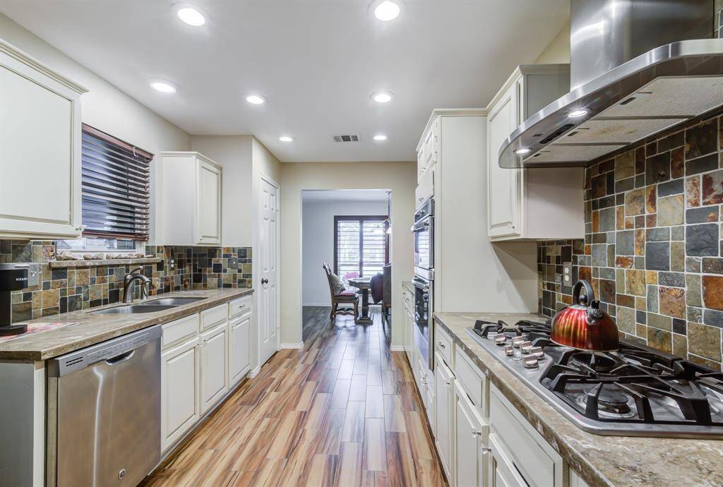 Modern kitchen with sleek stainless steel appliances, beautiful tile backsplash, and wood-style flooring. Ample cabinet space and a cozy dining area visible in the background.