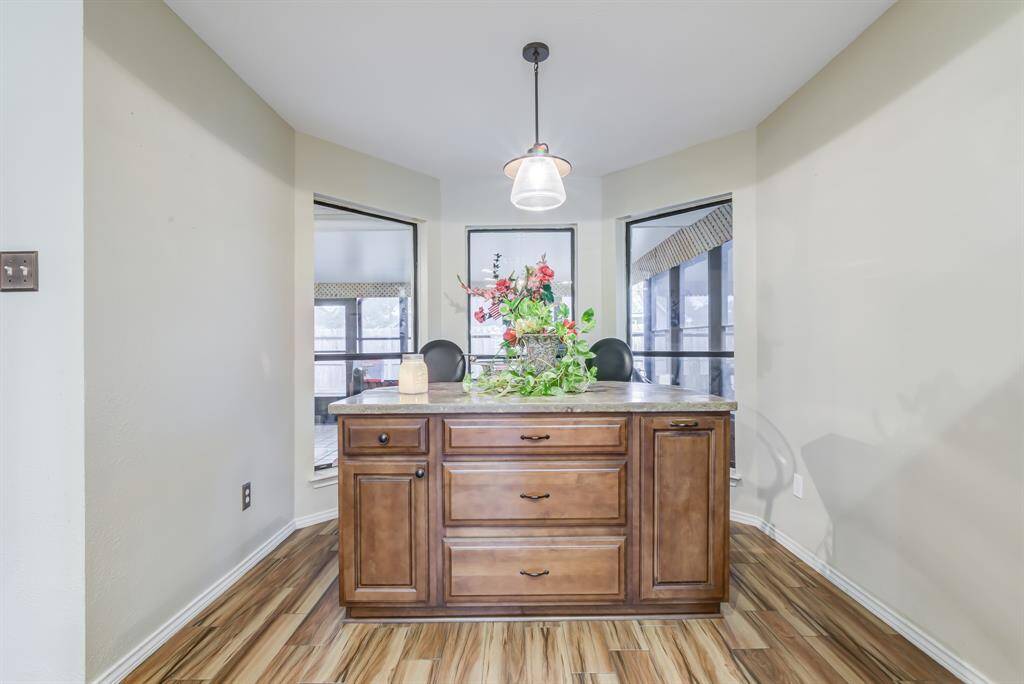 This photo showcases a cozy breakfast area with a central wooden island featuring storage drawers, elegant lighting, and large windows providing ample natural light. The space is perfect for entertaining or enjoying meals.