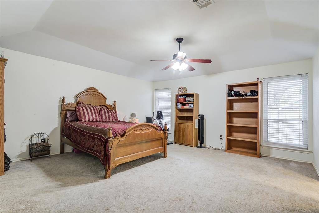 Spacious bedroom with a vaulted ceiling, featuring a ceiling fan, large windows for natural light, and carpeted flooring.