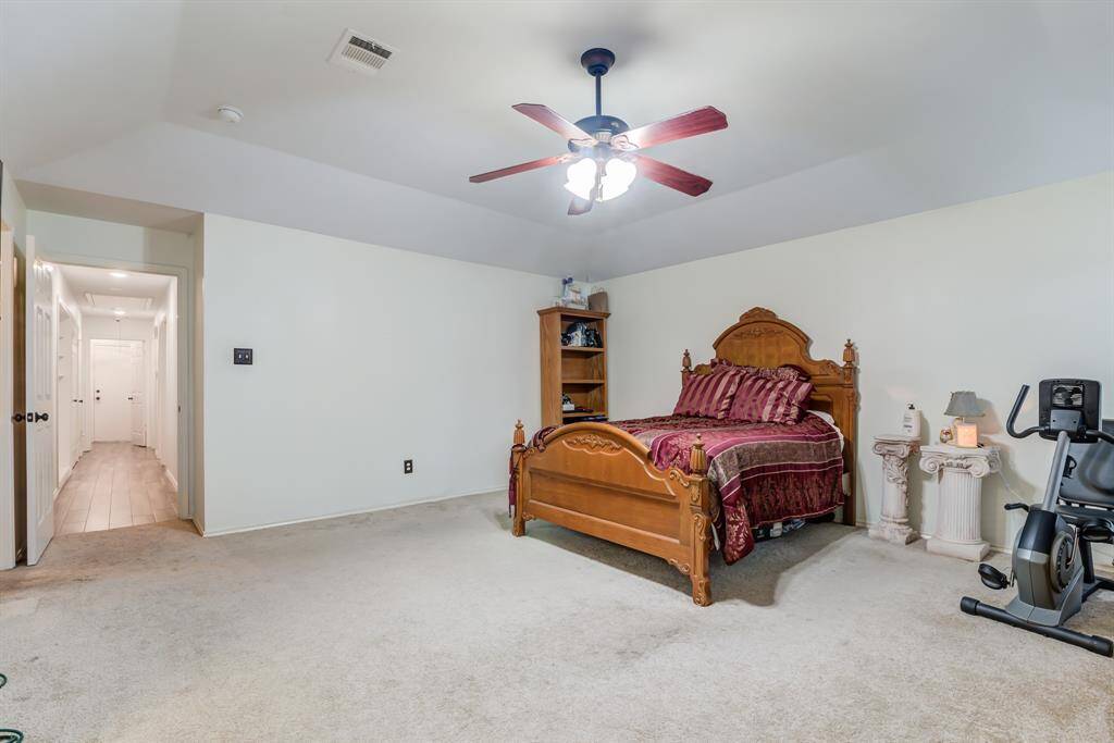 Primary bedroom features a spacious layout with a ceiling fan, neutral walls, and carpet flooring.