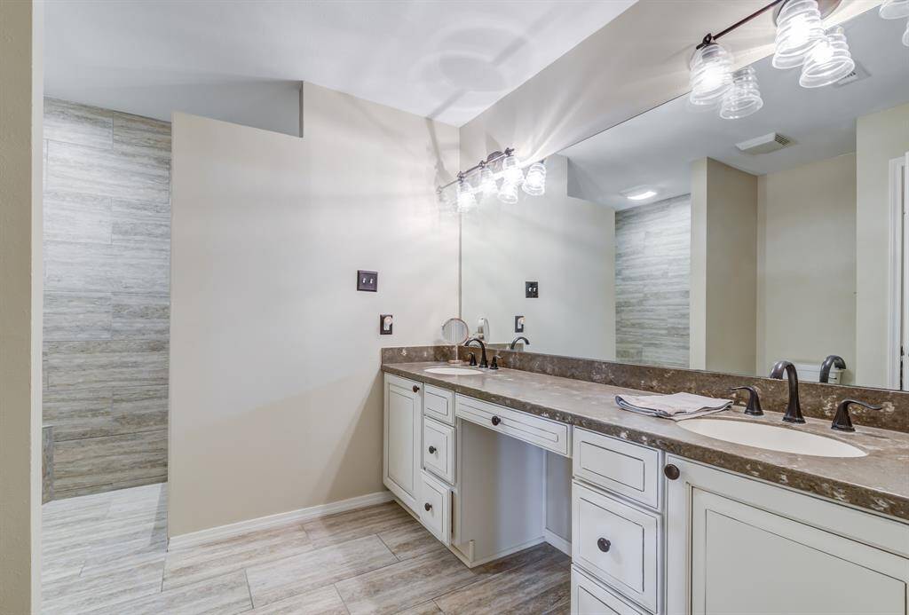Primary bathroom features a spacious dual-sink vanity with elegant fixtures and ample cabinet storage. The neutral tones and large mirror enhance the room's brightness, while the tiled shower adds a modern touch.