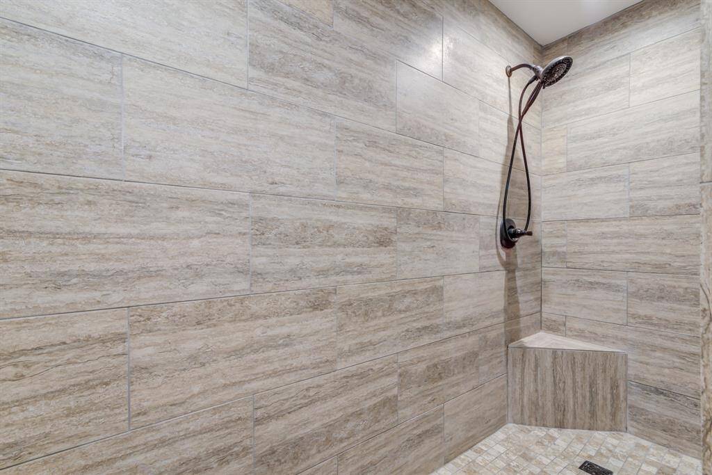 Modern shower with large, neutral-toned tiles and a sleek showerhead. The design includes a built-in corner bench, providing comfort and functionality.