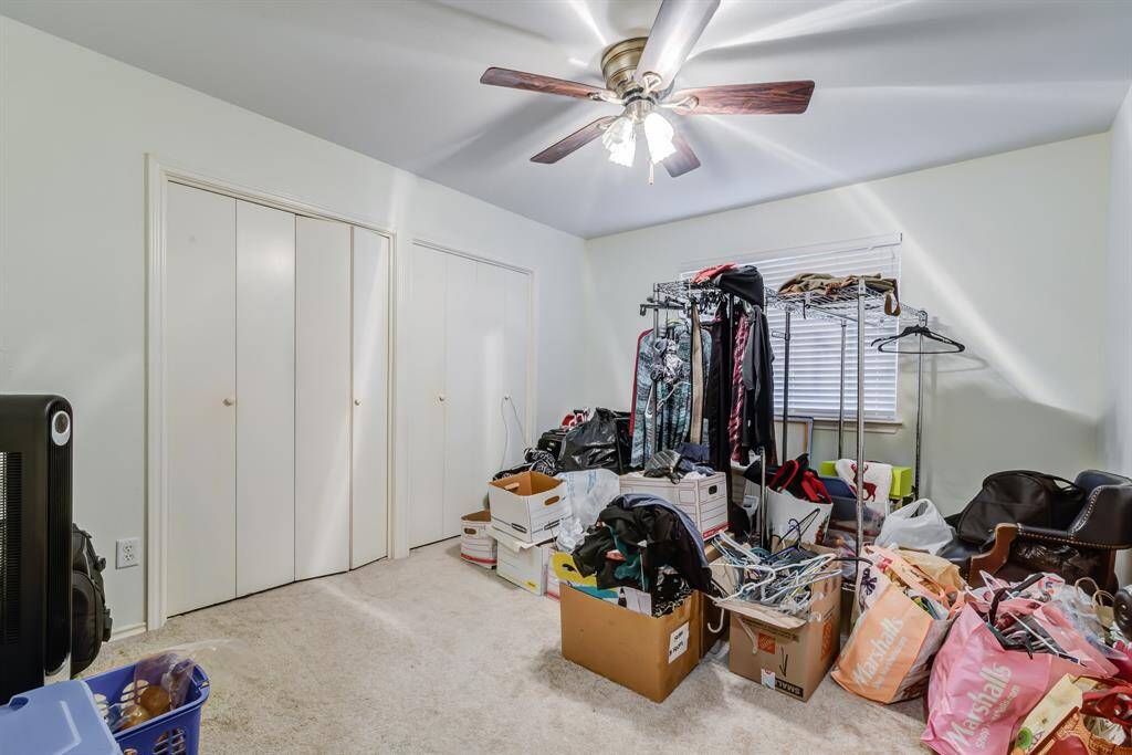 Third bedroom with carpeted flooring, a ceiling fan, and ample closet space. The room is currently used for storage.