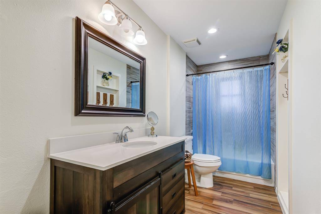 This bathroom features a stylish dark wood vanity with a large framed mirror, modern light fixtures, wood-style flooring, and a tub/shower combo.