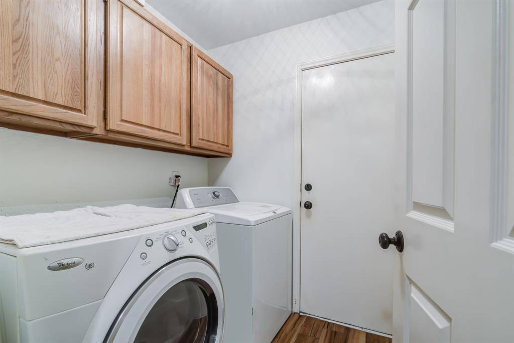 A compact laundry room featuring a front-loading washer and top-loading dryer, with wooden cabinets for storage. The space is bright with a clean, practical layout.