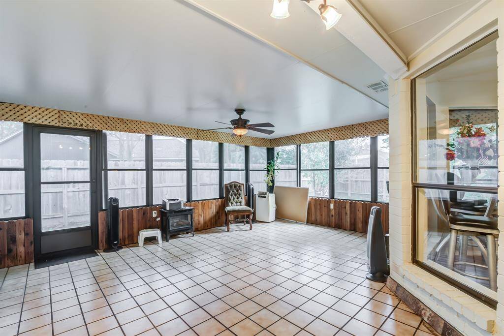 This photo showcases a bright, spacious sunroom with large windows, a ceiling fan, and tiled flooring. The room features wood accents and offers ample natural light, making it perfect for relaxation or entertaining. The room does have central heating and cooling.