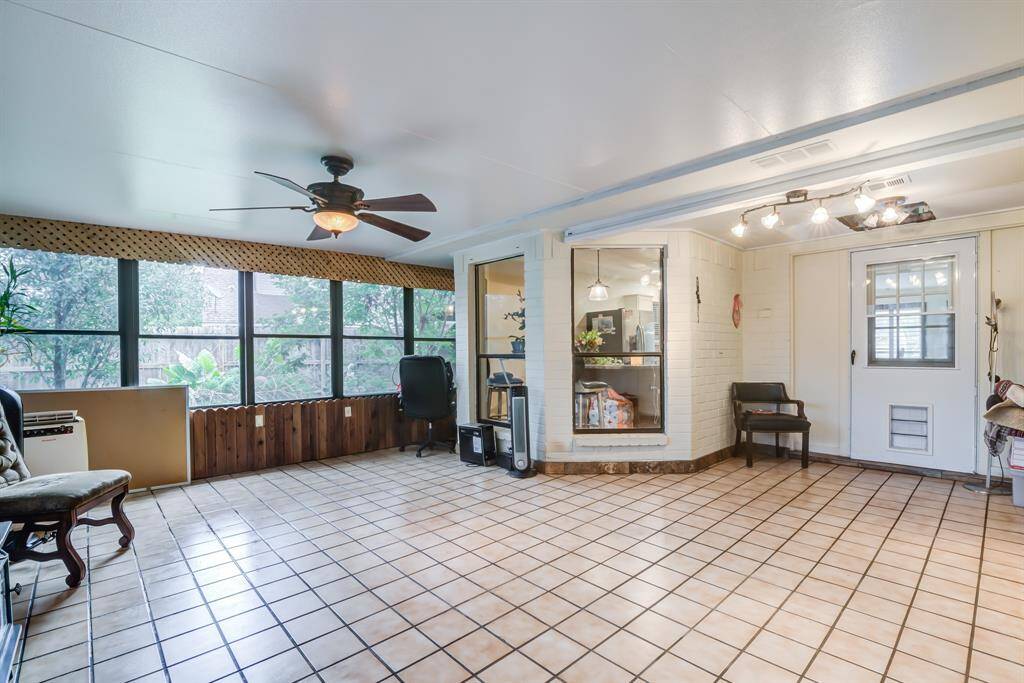 This spacious sunroom features large windows for natural light, a ceiling fan, and tile flooring. It's an inviting space for relaxation or entertaining, with views of the garden outside.