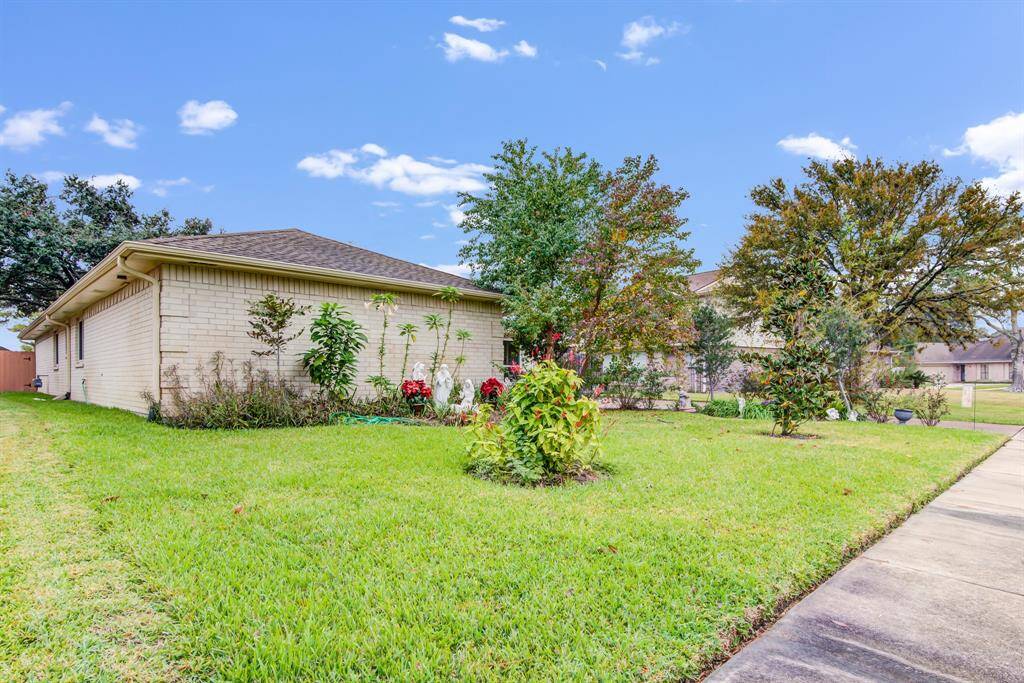 Charming brick home with a spacious, well-maintained front yard featuring lush greenery and mature trees. The property offers a peaceful suburban setting with a sidewalk leading to the entrance.