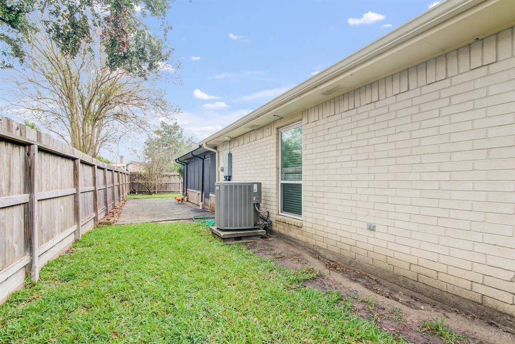 The photo shows a side view of a house with a white brick exterior, featuring a small grassy yard and a wooden fence.
