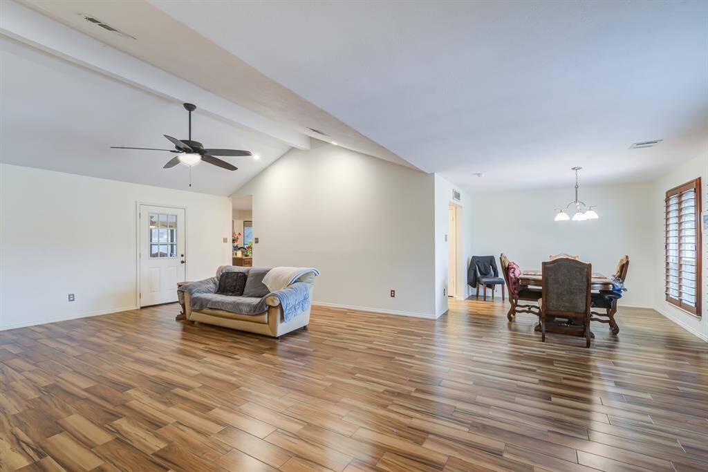 This spacious open-concept living and dining area features beautiful wood-like flooring, a ceiling fan, and ample natural light from large windows. The room's layout offers flexibility for furniture arrangement and an inviting atmosphere for entertaining.