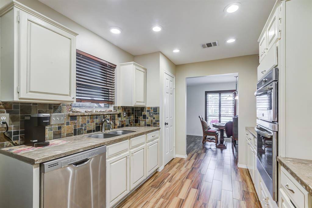Bright kitchen with modern appliances, tiled backsplash, and wood-look flooring. Opens to a dining area with natural light.