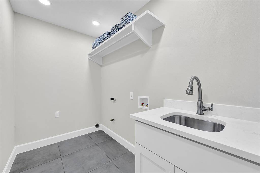 This newly designed utility room features a built-in sink, sleek quartz countertops, and a spacious shelving and hanging area for added convenience. With modern tile flooring and recessed lighting, this functional space is perfect for laundry and additional storage needs.