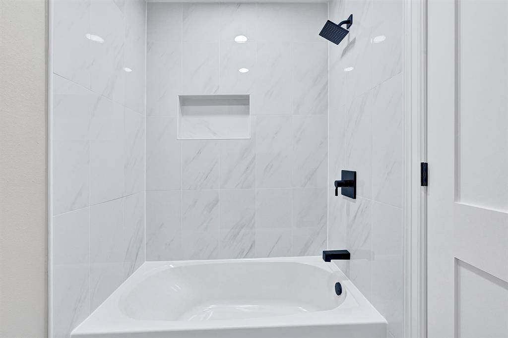 This newly designed shower features floor-to-ceiling sleek marble-look tiles, creating a spa-like retreat with a modern touch. The built-in shower niche and matte black fixtures add both style and functionality, enhancing the elegance of this space.
