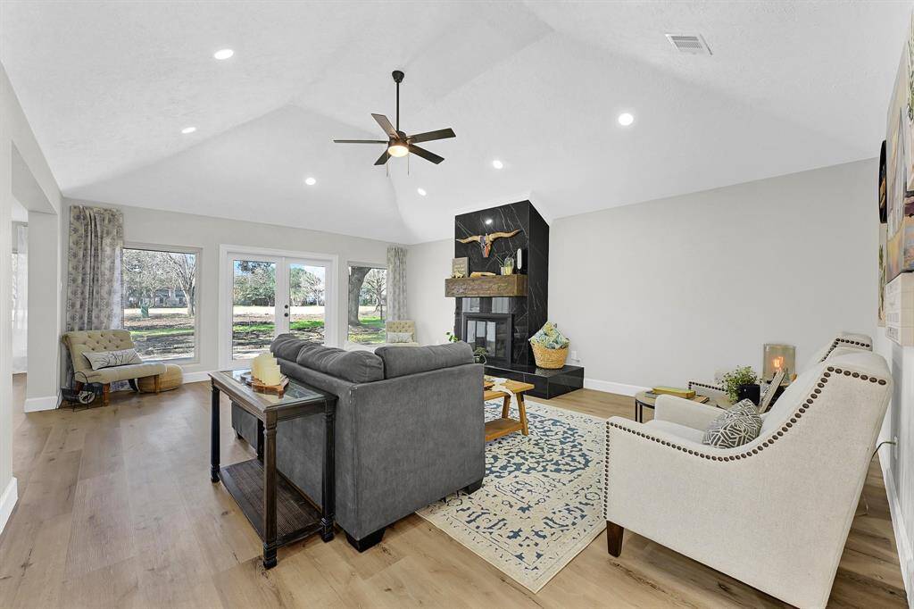 The spacious living room is filled with natural light, featuring a coved ceiling, vinyl plank flooring, and a striking black freestanding fireplace that serves as a bold focal point. The expansive windows offer breathtaking views of the lush outdoors, creating a seamless connection between the interior and nature. The open layout makes the space both inviting and functional for everyday living and entertaining.