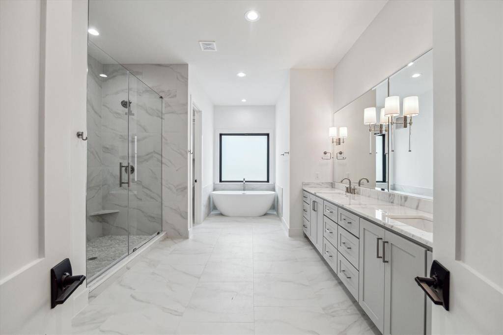 Sumptuous primary bath features Tesoro Bianco quartz counter double sink vanity, ceramic tile floors / shower stall with shower fixture and handheld shower wand, large and 67" soaking tub.