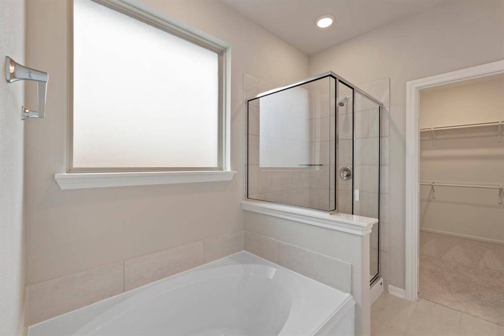 This additional view of your primary bathroom features tile flooring, fresh paint, walk-in shower, a separate garden tub, and a large walk-in closet.