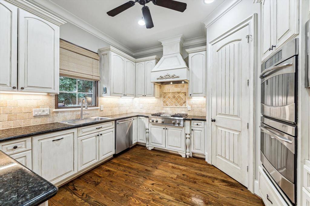 The well-equipped kitchen features a large walk-in pantry, granite countertops, a tumbled travertine backsplash, bar seating, and custom cabinetry with under-cabinet lighting. High-end appliances include GE Profile double ovens, a GE Monogram built-in refrigerator/freezer, and a 4-burner gas cooktop with a griddle and vent hood above.