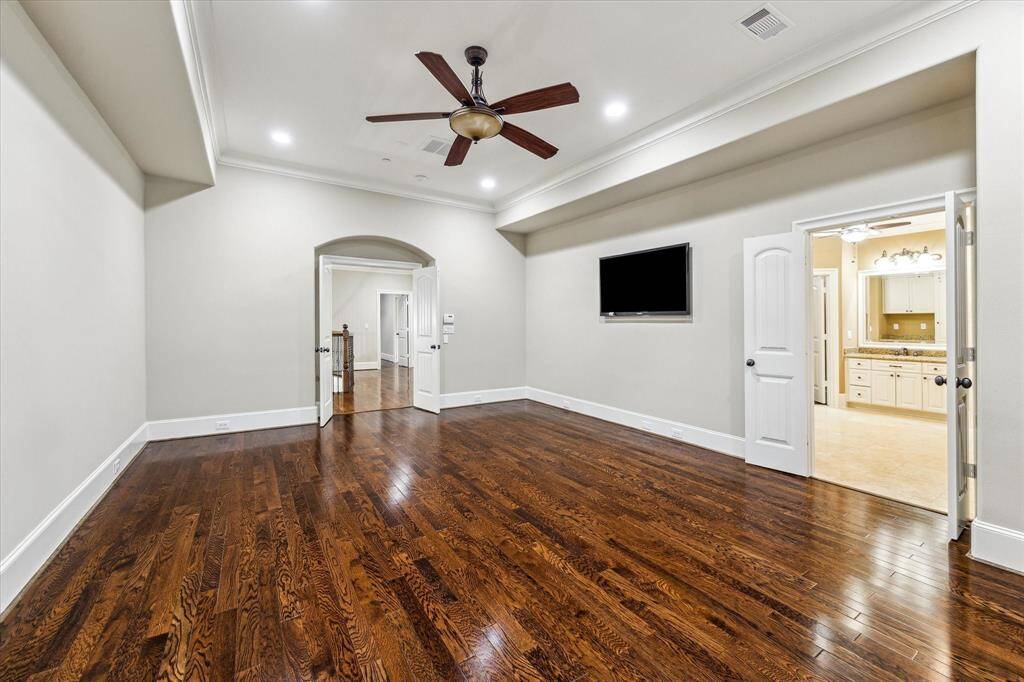 An arched entryway with double doors leads into the spacious primary suite, where rich hardwood floors continue throughout the upstairs. Features include a 10’2” tray ceiling with a ceiling fan and double doors opening to the spa-like bath.