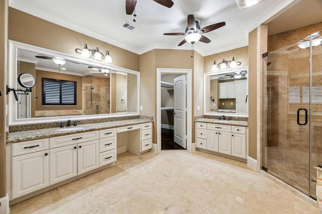 The spa-like primary bath features polished travertine floors, dual vanities with granite countertops, a built-in kneehole vanity, and a large jetted tub with a tile surround. A frameless glass walk-in shower and an expansive walk-in closet complete this luxurious retreat.
