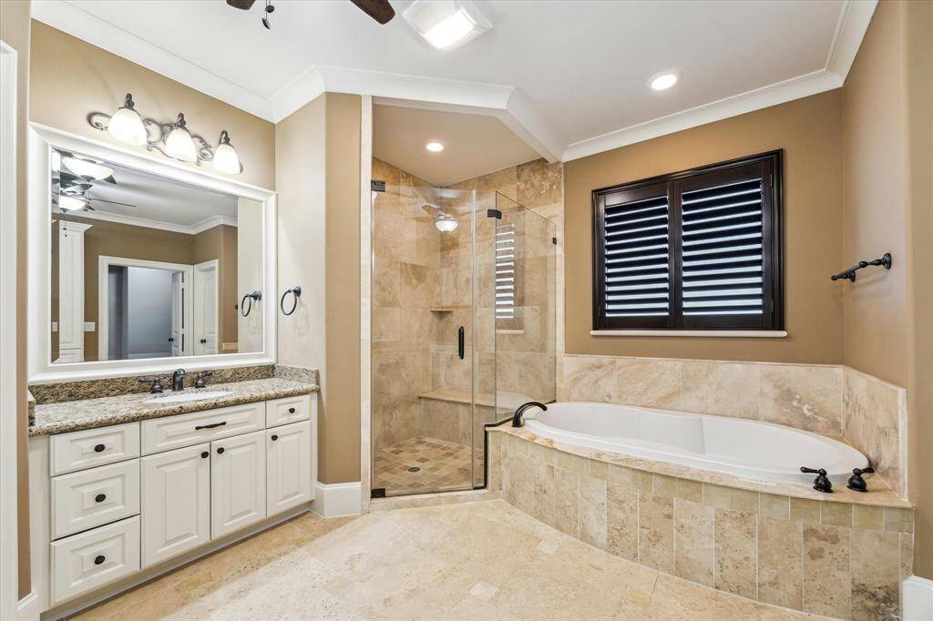 Another view of the primary bath highlights the jetted tub with a tile surround + large window with plantation shutters, and a frameless glass walk-in shower with a built-in bench.