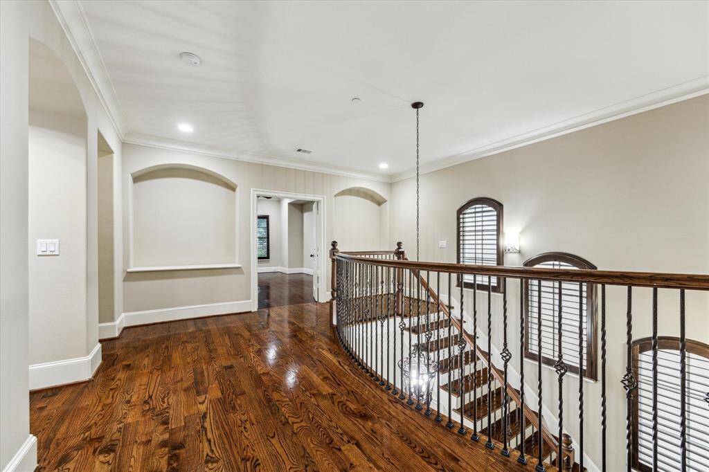 A staircase with wood treads and large arched windows with plantation shutters leads to the second-floor landing, which showcases art niches and elegant iron railings while providing access to the elevator closet, secondary bedrooms, and double doors to the primary suite.