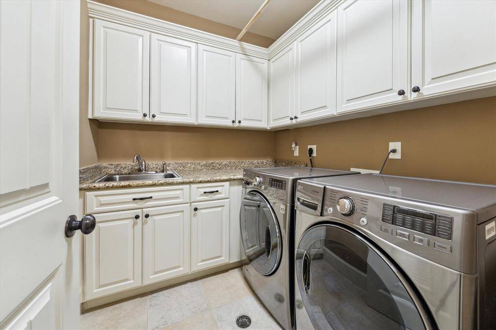 Located on the second floor, this oversized utility room features a full-sized LG washer and dryer, granite counter with stainless-steel sink, and cabinet storage above and below.