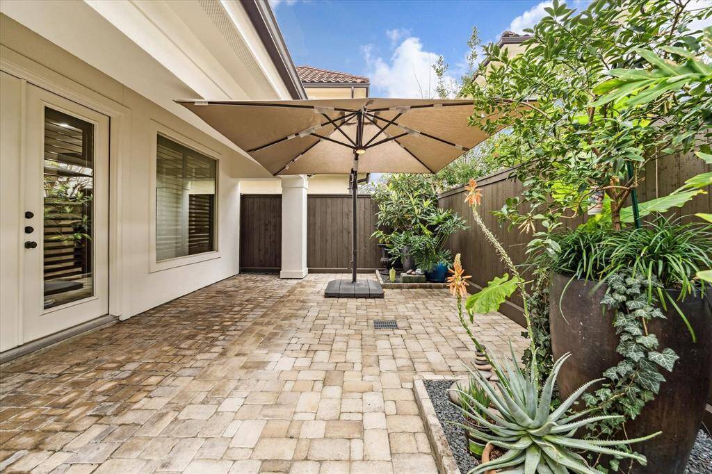 The paved backyard offers a low-maintenance outdoor retreat with a covered patio, oversized cantilever umbrella, lush landscaping, and a fully fenced perimeter (2024).
