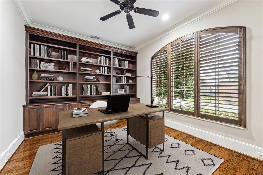 Behind double glass-paneled doors, this elegant study features a wall-to-wall custom built-in bookcase, rich hardwood floors, and an arched window with plantation shutters overlooking the front yard—creating a refined and functional workspace. This photo has been virtually staged.